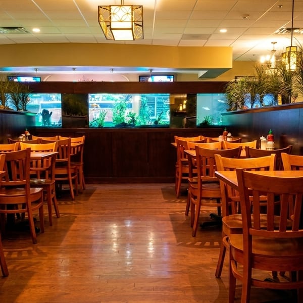 Restaurant dining room with wooden tables and chairs, aquariums, and hanging light fixtures.