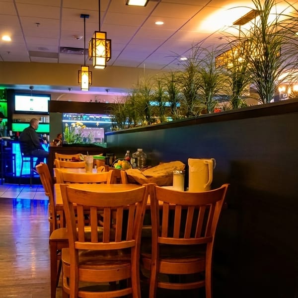 Restaurant interior with wooden tables and chairs, a bar with blue lighting, and decorative plants.
