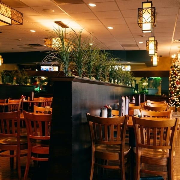 Restaurant interior with wooden tables and chairs, decorative plants, and a Christmas tree in the background.