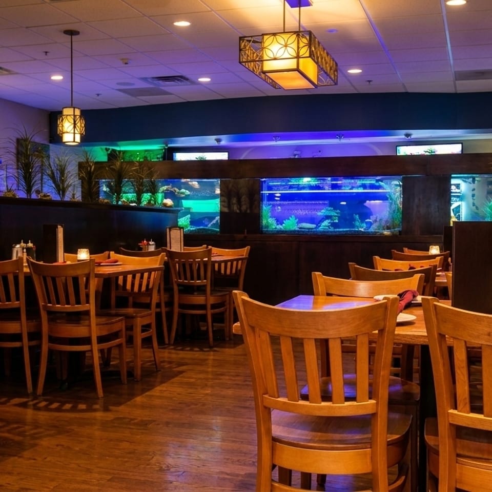 Restaurant dining room with wooden tables and chairs, illuminated aquariums, and decorative plants.