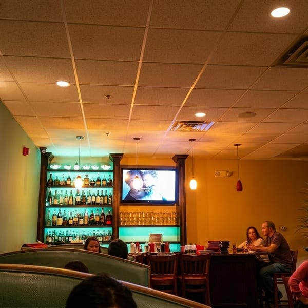 A restaurant interior with booths, a bar, liquor shelves, and patrons dining.