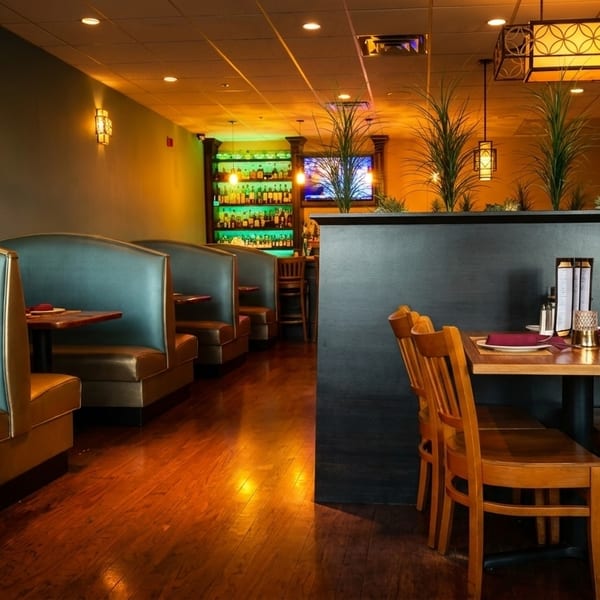 Restaurant interior with teal booths, wooden tables, chairs, and a bar with colorful lighting.